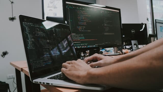 Coding.jpg 複数の画面にコードを表示しながらノートパソコンで作業する様子
